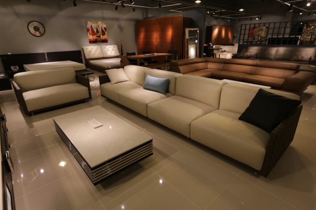 Modern showroom interior showcasing commercial track lighting casting warm white illumination over a luxury furniture display, featuring cream leather sectional sofas and contemporary home decor