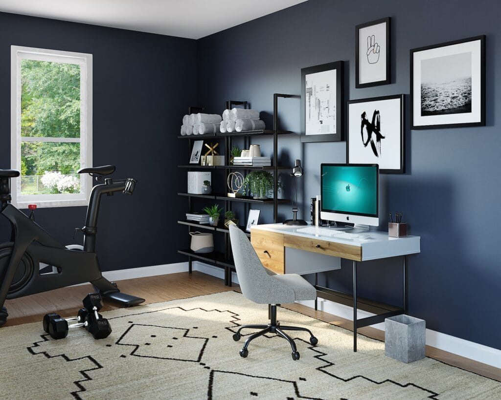 A modern multi-functional home office and gym space featuring deep navy blue walls, light wood flooring, and a large patterned area rug. A sleek white and wood desk with an iMac computer and grey swivel chair sits against the wall, next to a black metal shelving unit and a stationary exercise bike with dumbbells in the foreground
